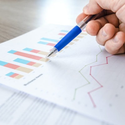 white professional woman's hand using a pen to review bar charts