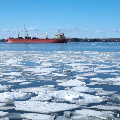 a red icebreaker boat (in background along horizon) on a body of water with floating ice in the foreground