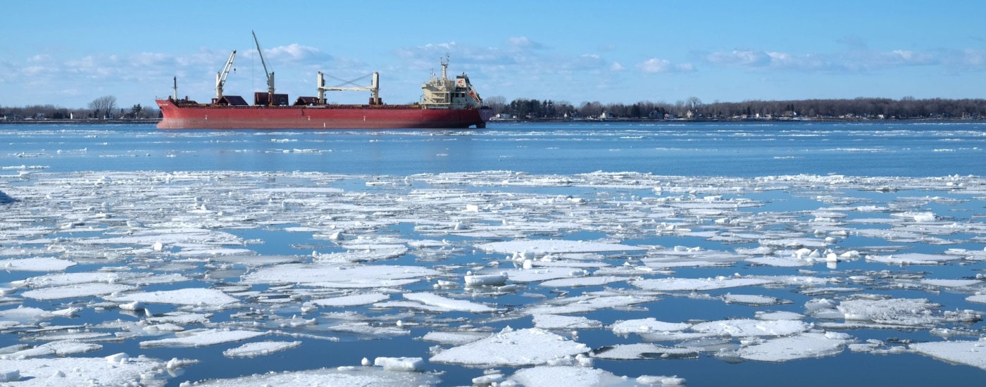 a red icebreaker boat (in background along horizon) on a body of water with floating ice in the foreground