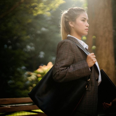young professional woman carries a bag to her interview; she is wearing a suit, a white blouse, and has her hair in a ponytail