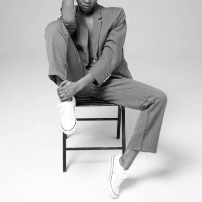 professional woman wears a suit and sneakers; she is sitting on a chair with one leg drawn up.