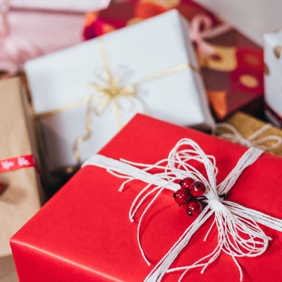 a collection of wrapped gifts in different wrapping paper and with different bows; the topmost gift has some cranberries near the bow
