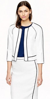 woman wears white linen herringbone jacket and skirt, with a dark top beneath the jacket