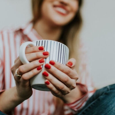 young professional woman holds coffee cup; she has short red nails