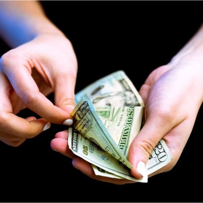 woman looks through a pile of cash; she is wearing white nail polish