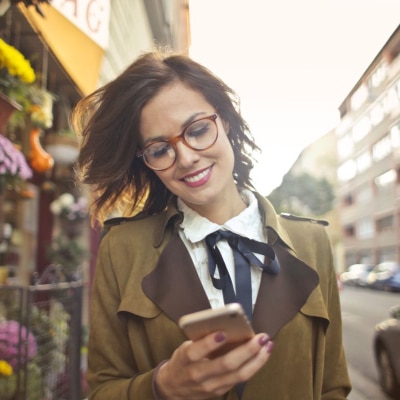 young professional woman walking along a city street; she is looking at her phone to read this post on what not to wear as a summer associate