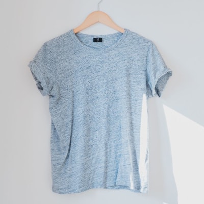 A light blue T-shirt (possibly worn but not dirty!) hanging on a wooden hanger against a white wall