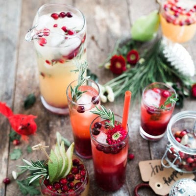 festive holiday drinks are photographed from above; the brown table decorated with green sprigs is visible