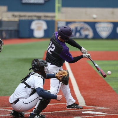 baseball player swings at a pitch while an umpire and catcher look on