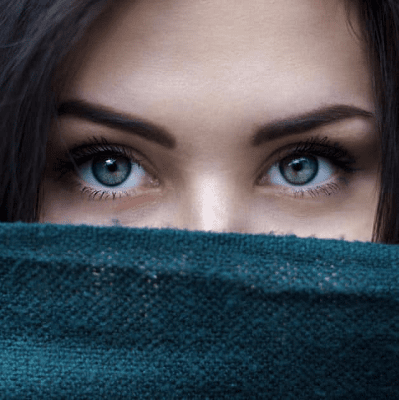 close-up of woman's greenish eyes; she has brown hair and is covering the lower part of her face with a teal turtleneck, scarf or blanket