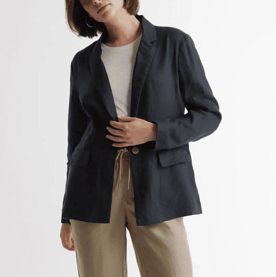 woman tilts head while wearing a navy linen blazer, beige pants, and a white tee