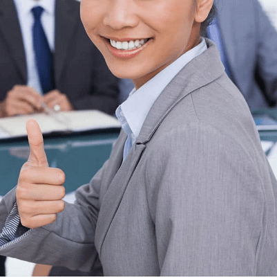professional woman in suit sits across table from two men and a woman in suits; the woman in the foreground is giving a thumb's up and a smile because her on-campus interview is going well