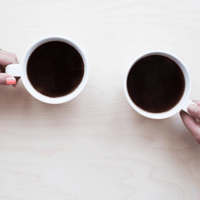 two women hold coffee cups up as if to cheers; view is aerial